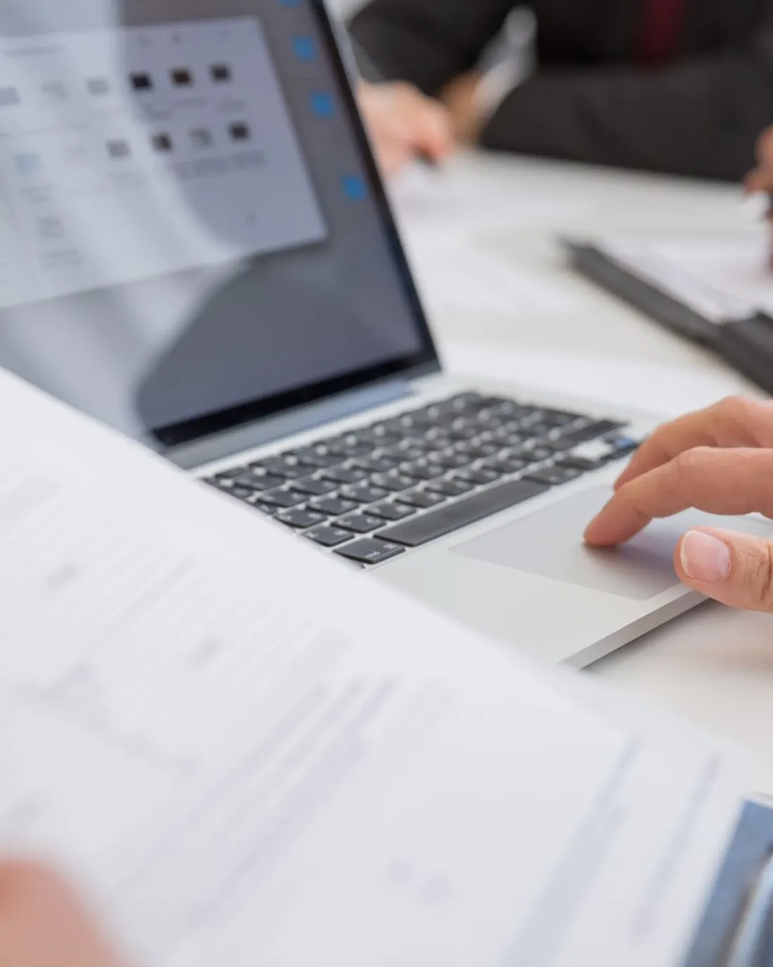 Manos trabajando sobre documentos y un portátil en la mesa del despacho